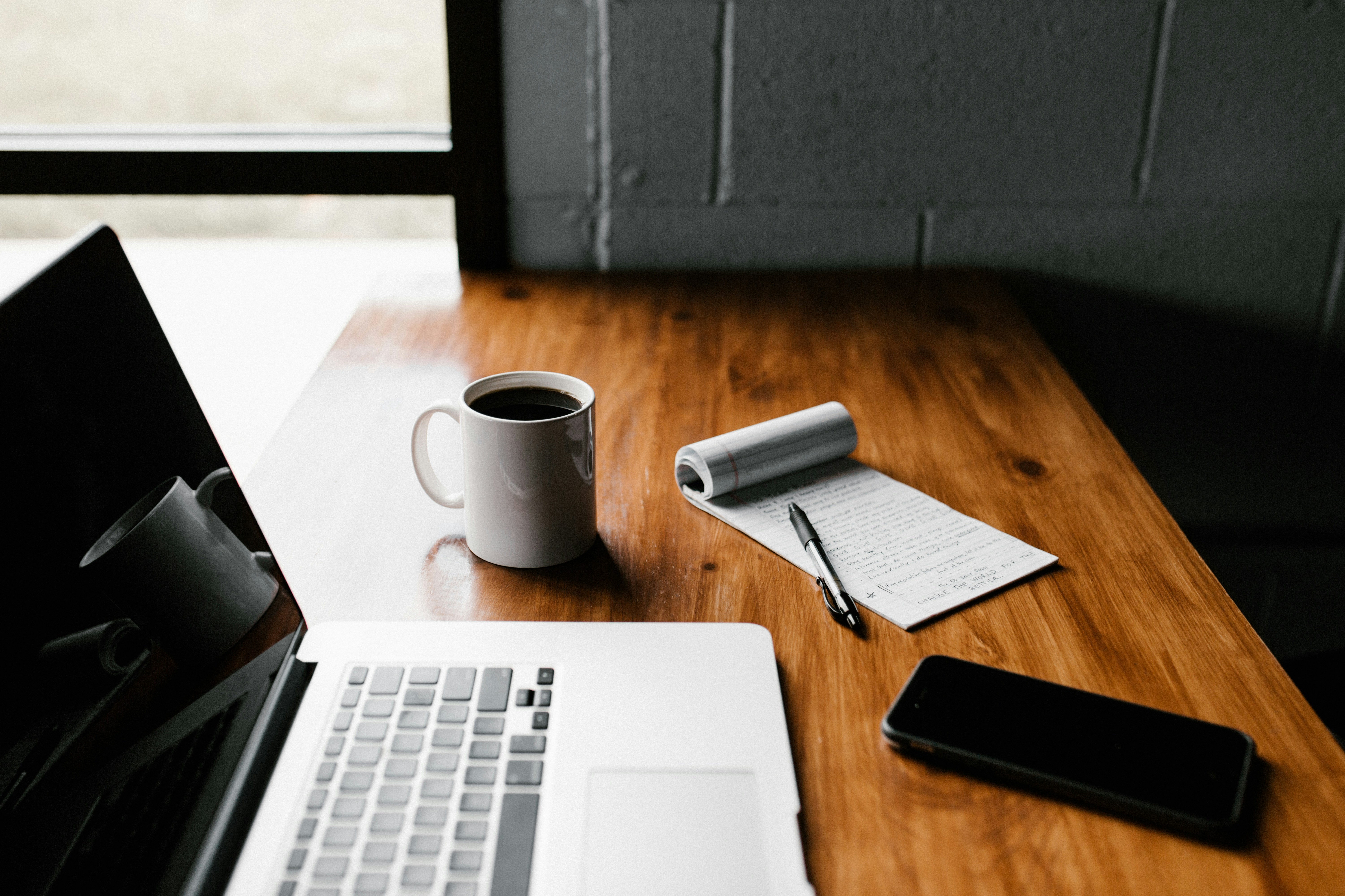 Laptop, notebook, and coffee mug on wooden desk